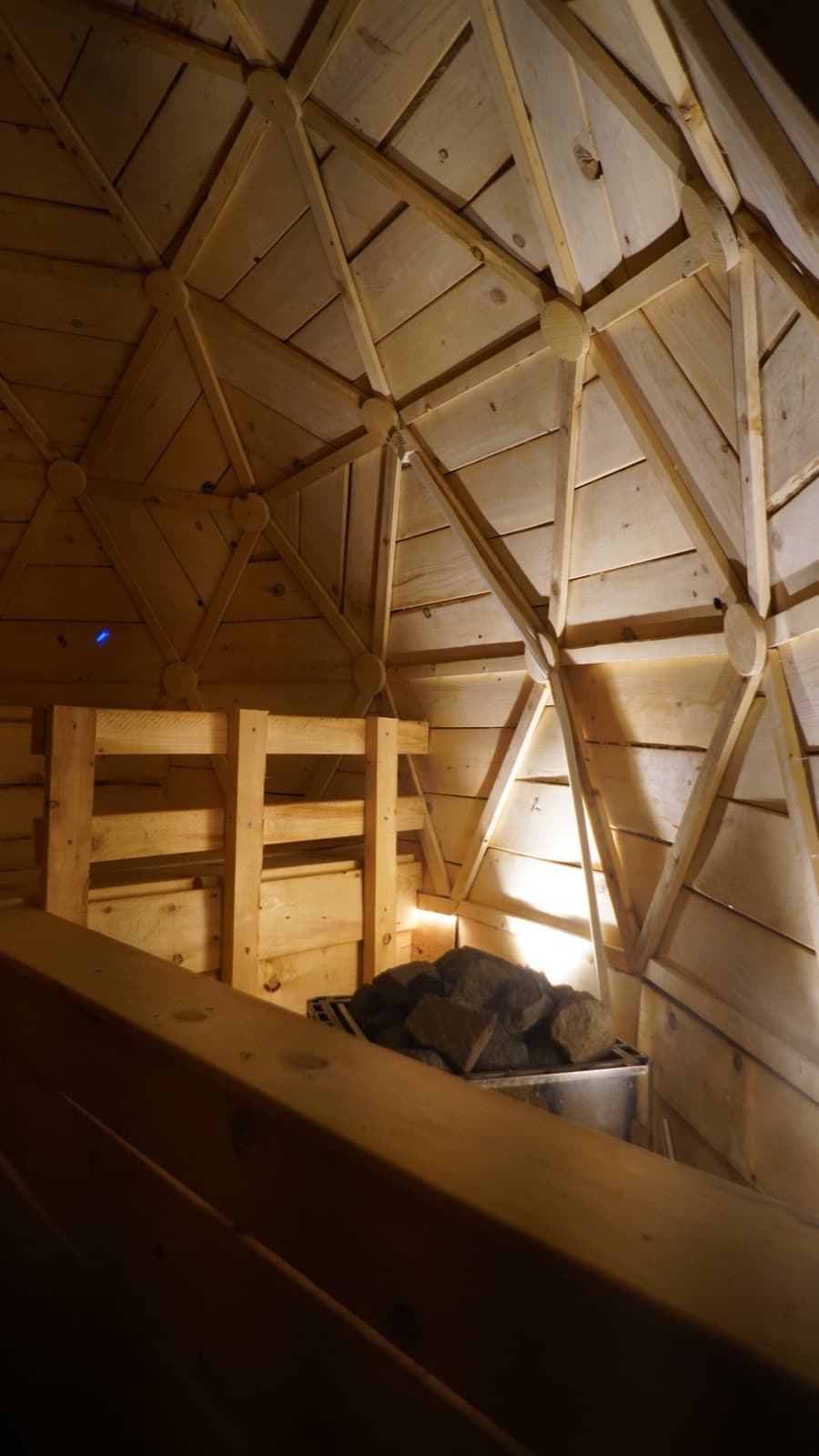 Inside the wooden geodesic dome — benches and the stone stove