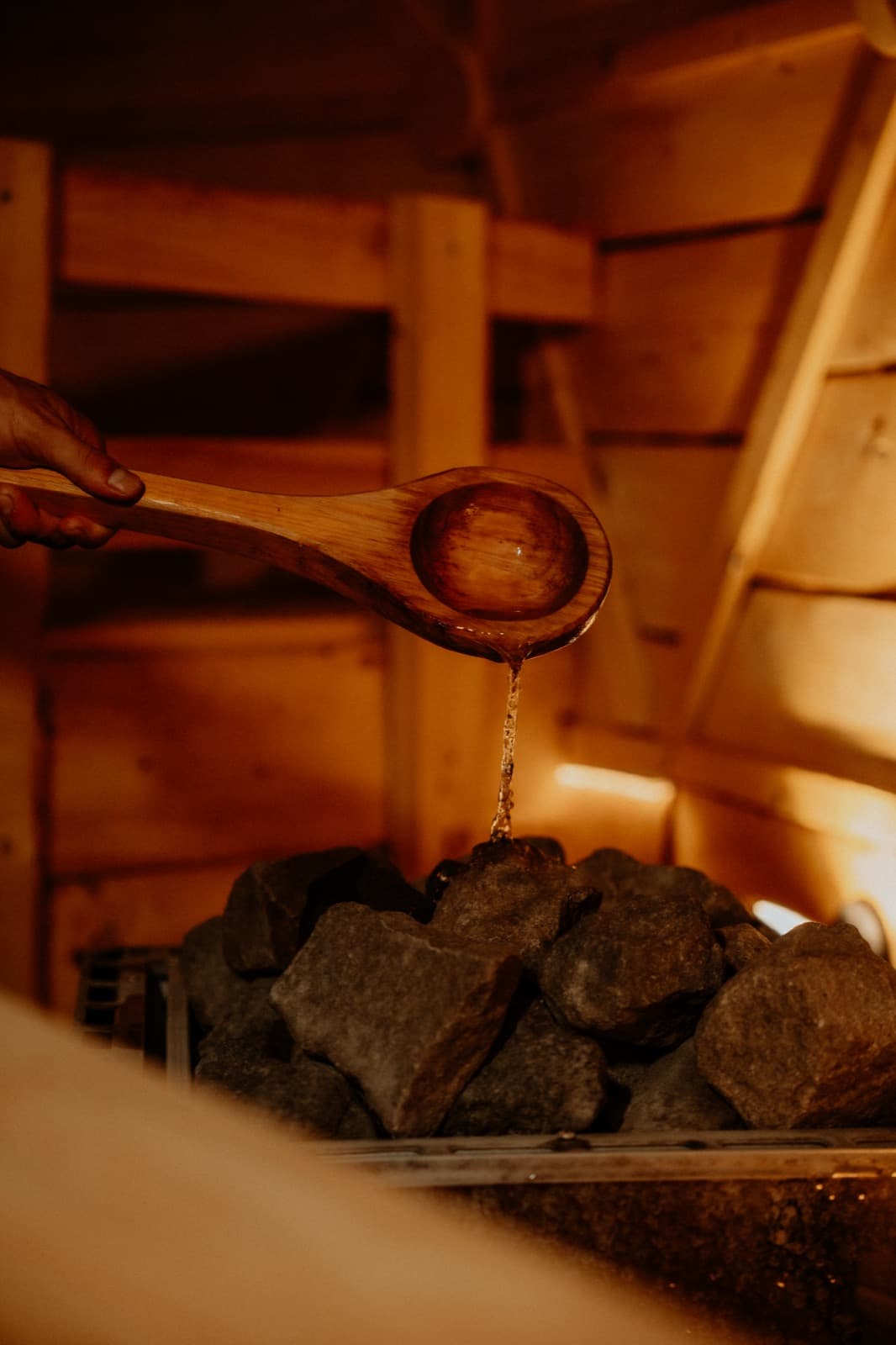 Herbal brew pouring from the wooden ladle onto the hot stones